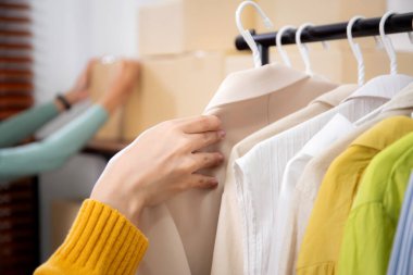 Hazırlık teslimatı için mağazada kıyafet düzenleyen genç bir kadın, satıcı seçici giysiler, perakende satış için seçici kıyafetler, teslimat için mal, küçük işletme.