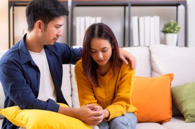 Asyalı genç adam, üzgün kadını nazikçe kucaklayarak rahatlatıyor. Oturma odasındaki kanepede oturan kadın, ifadesiyle mutsuz ve endişeli bir eş. Kocası ise şefkat ve yakınlıkla teselli ediyor..