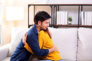 Genç Asyalı çift, evdeki oturma odasında sevgi dolu bir şekilde kanepede otururken birbirlerine sarılırlar. Karı koca, nazik ve sevgi dolu bir şekilde birbirlerine sarılırlar. Birbirlerine sarılırlar..