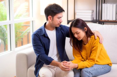 Asyalı genç adam, üzgün kadını nazikçe kucaklayarak rahatlatıyor. Oturma odasındaki kanepede oturan kadın, ifadesiyle mutsuz ve endişeli bir eş. Kocası ise şefkat ve yakınlıkla teselli ediyor..