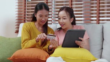 Kanepede oturan iki genç Asyalı kadın internet üzerinden tablet bilgisayar alışverişi yapıyor. İnternete kredi kartı satın alıyor, iş, alım ve ödeme, iş ve finans ile kadın ödemesi yapıyor..