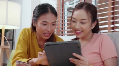 Kanepede oturan iki genç Asyalı kadın internet üzerinden tablet bilgisayar alışverişi yapıyor. İnternete kredi kartı satın alıyor, iş, alım ve ödeme, iş ve finans ile kadın ödemesi yapıyor..