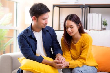 Asyalı genç adam, üzgün kadını nazikçe kucaklayarak rahatlatıyor. Oturma odasındaki kanepede oturan kadın, ifadesiyle mutsuz ve endişeli bir eş. Kocası ise şefkat ve yakınlıkla teselli ediyor..