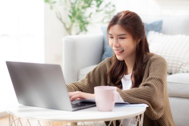 Genç Asyalı kadın evinde mutlu ve tatmin edici bir dizüstü bilgisayar kullanıyor, defter bilgisayarlı kadın rahatlaması ya da evden çalışıyor, iş gezisi e-postası, iş dünyası ve serbest çalışma.