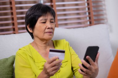 Kıdemli Asyalı kadın internet üzerinden akıllı telefon alışverişi yapıyor. İnternete kredi kartı alıyor. Akıllı telefon, alım-satım, ödeme, iş ve finans ile kadın ödemesi yapıyor..