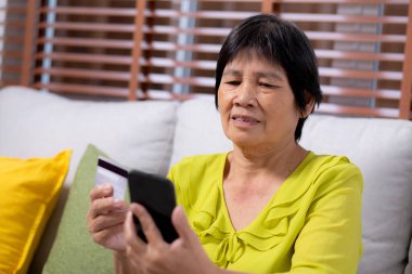 Kıdemli Asyalı kadın internet üzerinden akıllı telefon alışverişi yapıyor. İnternete kredi kartı alıyor. Akıllı telefon, alım-satım, ödeme, iş ve finans ile kadın ödemesi yapıyor..