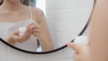 Genç bir kadının banyoda aynaya bakarken cildine krem sürmesi ya da losyon sürmesi, tedavi için nemlendirici sürmesi, yüz, güzellik ve cilt kırışıklıkları..