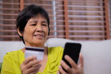 Kıdemli Asyalı kadın internet üzerinden akıllı telefon alışverişi yapıyor. İnternete kredi kartı alıyor. Akıllı telefon, alım-satım, ödeme, iş ve finans ile kadın ödemesi yapıyor..