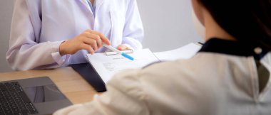 Genç Asyalı hasta kadın, modern tıp bürosundaki belgeye bakarken, cilt ve kırışıklıkları hakkında doktorla görüşüyor, doktor yüz tanılarını ve açıklamalarını yapıyor..