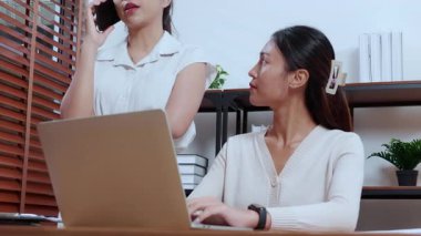 İki genç Asyalı iş kadını pazarlama ve finans hakkında planlama ve strateji yaparken, iş arkadaşları da akıllı telefon, toplantı ve dizüstü bilgisayarda ortaklık, iş ve danışmanlık konularında konuşuyorlar..