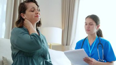 Hasta bakıcı kanepede oturup hasta kadına sağlık kontrolü ve teşhiste bulunurken evdeki kaslı boyun ağrısı, kanepede oturan hademe hasta kadını, sigortayı ve tıbbi muayeneyi kontrol ediyor..