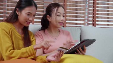 Kanepede oturan iki genç Asyalı kadın internet üzerinden tablet bilgisayar alışverişi yapıyor. İnternete kredi kartı satın alıyor, iş, alım ve ödeme, iş ve finans ile kadın ödemesi yapıyor..