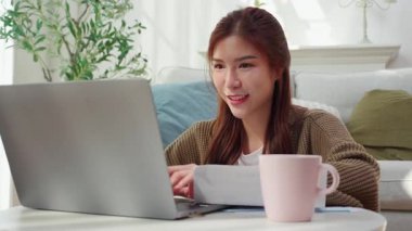 Genç Asyalı kadın evinde mutlu ve tatmin edici bir dizüstü bilgisayar kullanıyor, defter bilgisayarlı kadın rahatlaması ya da evden çalışıyor, iş gezisi e-postası, iş dünyası ve serbest çalışma.