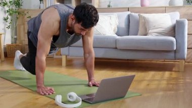 Genç Asyalı adam evde antrenman yapıyor. Evde dizüstü bilgisayarla ev bilgisayarı izliyor. Oturma odasında, sağlık, sağlıklı yaşam tarzı ve egzersiz için vücut gücü saptadı ve motive etti..