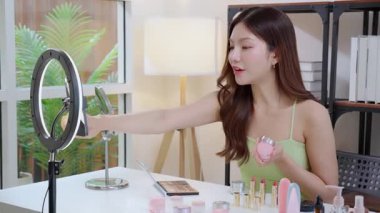 Genç Asyalı kadın kozmetik ürünlerini sosyal medya platformunda takipçiler, krem ya da losyonu canlı yayında inceleyen, etkileyen ve gözden geçiren kadınlar için heyecan verici bir şekilde sunup gözden geçiriyor..