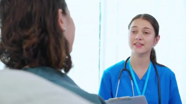 Bakıcı kanepeye oturup kadın hastaya evdeki sağlıkla ilgili sağlık kontrolü ve teşhisi koyuyor. Bekçi kanepede oturuyor. Kadını, sigortayı ve sağlık durumunu izah ediyor..