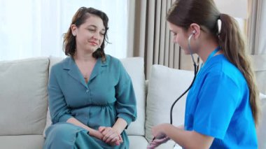 Bakıcı genç hemşire. Steteskoplu kadını muayene ediyor. Oturma odasındaki kanepede oturuyor..