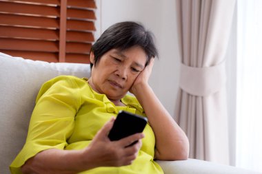 Kıdemli Asyalı kadın evdeki akıllı telefona bakarken koltukta oturup endişeleniyor ve strese giriyor. Mutsuz ve endişeli bir kadın akıllı telefondan, yaşam tarzından ve iletişimden izliyor..
