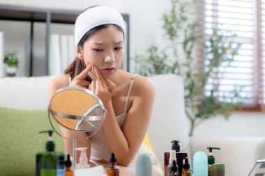 Genç Asyalı kadın, yüz bakımı stresi ile aynaya bakıyor. Oturma odasındaki kanepede oturuyor. Cilt bakımı, cilt bakımı, cilt bakımı, cilt bakımı ve cilt bakımı..