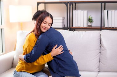 Genç Asyalı çift, evdeki oturma odasında sevgi dolu bir şekilde kanepede otururken birbirlerine sarılırlar. Karı koca, nazik ve sevgi dolu bir şekilde birbirlerine sarılırlar. Birbirlerine sarılırlar..