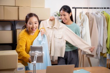 İki genç Asyalı kadın online giyim mağazasında yaşarken, evde sosyal tabletle giysi satışı yaparken, girişimci çevrimiçi kıyafet satışı ve sunumu için çevrimiçi satış yapıyor..