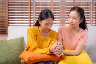 Genç Asyalı bir kadın, arkadaşını ağlama ve depresyonla rahatlatırken oturma odasında kanepede oturuyor, arkadaşlığın sıkıntısı ve empatisi, umutsuzluk ve ruh sağlığını desteklerken, bir kadın da arkadaşını teşvik ediyor..