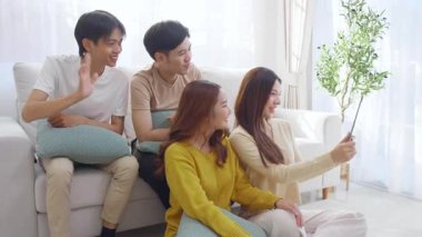 Genç Asyalı arkadaşlar evdeki oturma odasında dijital tablet kullanarak selfie ya da video çekiyorlar. Sosyal medya, etkileşim ve arkadaşlıkla bağlantı kurarken neşeli ve gülümsüyorlar..