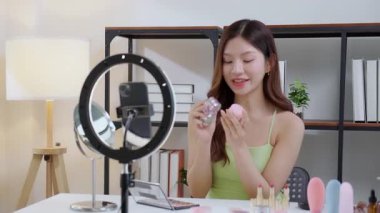 Genç Asyalı kadın kozmetik ürünlerini sosyal medya platformunda takipçiler, krem ya da losyonu canlı yayında inceleyen, etkileyen ve gözden geçiren kadınlar için heyecan verici bir şekilde sunup gözden geçiriyor..