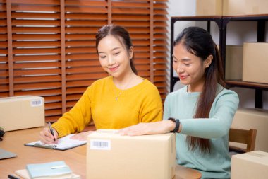 Çevrimiçi iş planlarken çalışan iki genç Asyalı kadın ve evdeki evrak işleri ile siparişleri kontrol etmek, çevrimiçi satıcı ile perakende satış, girişim işi ve kargo, nakliye ve hizmet.