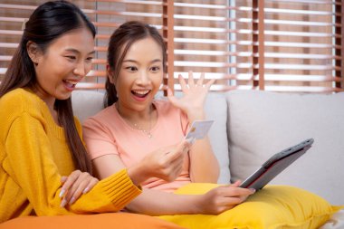 Kanepede oturan iki genç Asyalı kadın internet üzerinden tablet bilgisayar alışverişi yapıyor. İnternete kredi kartı satın alıyor, iş, alım ve ödeme, iş ve finans ile kadın ödemesi yapıyor..