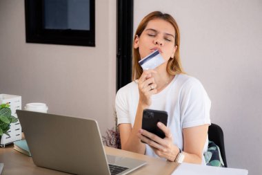 Kredi kartı ya da banka kartı tutan mutlu beyaz kadın akıllı telefon kullanırken internet üzerinden alışveriş yaparak ödeme yapıyor, finans, iş ve mali işlemler yaparak harcama yapan kadın.