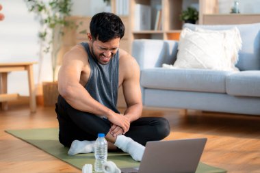 Evde antrenman yaptıktan sonra yoga minderinde oturan yorgun Asyalı genç adam evdeki terini siliyor. Egzersiz yaptıktan sonra laptopunu rahat, özgüvenli ve rahat bir şekilde izliyor..