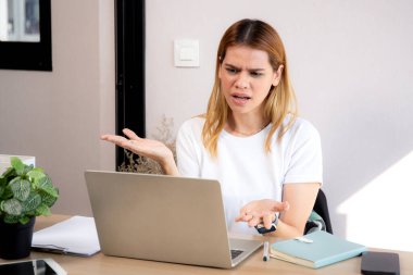 Mutsuz Kafkasyalı genç iş kadını masadaki dizüstü bilgisayarını kullanıyor. Ofiste stresli ve bitkin durumda. İş kadını hayal kırıklığına uğramış ve kaygılı bir şekilde dizüstü bilgisayarda çalışıyor..