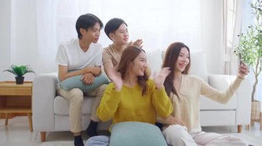 Bir grup Asyalı genç arkadaş kanepeye oturmuş evdeki akıllı telefonları kullanıyor. Sosyal medya, etkileşim ve arkadaşlıkla bağlantı kurarken neşeli ve gülümsüyorlar..