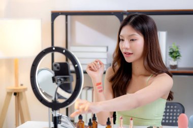 Genç Asyalı güzellik etkileyicisi, evde makyaj incelemesi yaparken kolunda birden fazla ruj gölgesi test ederken, içerik yaratıcısının sosyal medyada kozmetik ürünü ve sunumu, güzellik ve bakım.