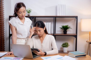 İki Asyalı iş kadını endişeli ve stresli bir şekilde dizüstü bilgisayar ve tablet üzerinde çalışıyor. İş hayatı, zihinsel sağlık, hayal kırıklığı, iş hayatı ve perişan durumdaki iş kadınlarından mutsuz..