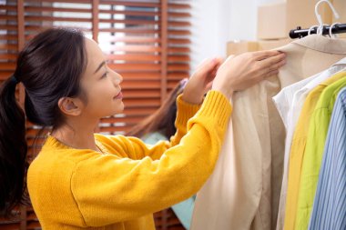 Hazırlık teslimatı için mağazada kıyafet düzenleyen iki genç Asyalı kadın, satıcı seçici giysiler, perakende satış için seçici giysiler, teslimat için mal, küçük işletme.