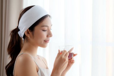 Saç bandı takmış, çay içen güzel, genç Asyalı bir kadın. Oturma odasından memnun, çay ya da içecek bir kadın. Sağlık ve rahatlama, yaşam tarzı ve sağlık için..