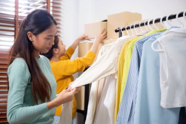 Hazırlık teslimatı için mağazada kıyafet düzenleyen iki genç Asyalı kadın, satıcı seçici giysiler, perakende satış için seçici giysiler, teslimat için mal, küçük işletme.