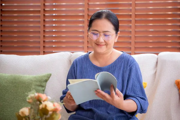 Asyalı son sınıf öğrencisi bir kadın kanepede oturmuş kitap okuyor. Oturma odasında dinleniyor. Yaşlı bir kadın hafta sonu rahat, hobi ve eğlence dolu bir kanepede edebiyat okuyor..