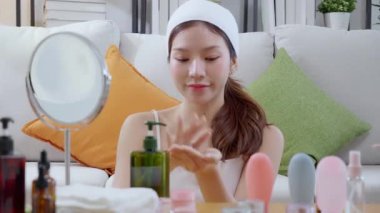 Güzel, genç Asyalı bir kadın ellerine losyon sürüyor. Evdeki aynaya bakıyor. Ellerine gençleştirme için güzellik serumu, kendine bakım, cilt bakımı ve sağlık için makyaj yapıyor..