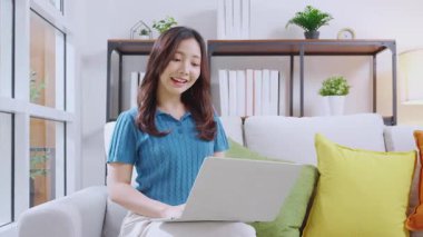 Kanepede oturan Asyalı genç bir kadın evdeki oturma odasında dizüstü bilgisayar kullanıyor, sosyal medyayı internet üzerinden sohbet ve sohbet için kullanıyor, yaşam tarzı kavramı..