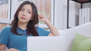 Genç Asyalı iş kadını laptopla çalışırken düşünceli bir şekilde ofisteki koltukta oturuyor, iş kadını evdeki not defterini kullanıyor, kadın dizüstü bilgisayarla düşünüyor..