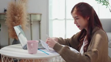 Mutlu Asyalı kadın dizüstü bilgisayar kullanarak ve belgeleri kontrol ederek gülümsüyor ya da evde, online bankacılık, bütçe ve gider planlama ve stratejisi, fatura veya vergi ve yatırım ile finans faturalarını kontrol ediyor..