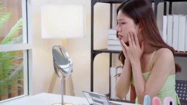 Genç Asyalı kadın endişeli görünüyor aynada incelenen surat, cilt problemi, yüz bakımı ve stres, endişe ve kırışıklık ile ilgili ifade, hoşnutsuzluk ve hüsranla.