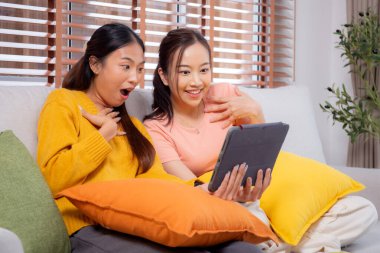 Oturma odasında dijital tablet kullanan iki genç Asyalı kadın, sosyal medyayı internet tableti ve konuşma mesafesi için kullanan kadın, yaşam tarzı kavramı.