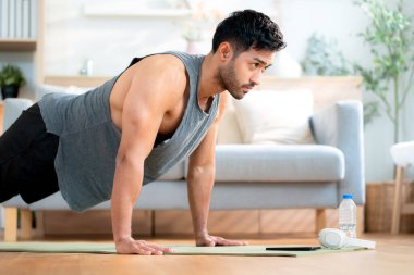 Genç Asyalı adam evde oturma odasında kararlılıkla şınav çekiyor yoga minderi eğitimi alıyor vücut geliştirme gücü ve sağlıklı yaşam tarzı için uygunluk, egzersiz rutini, kişisel bakım..