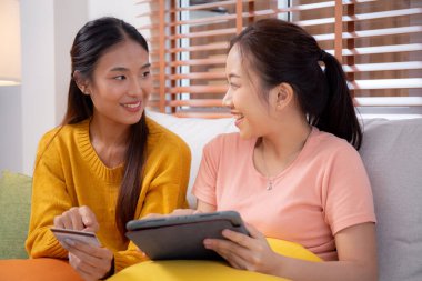 Kanepede oturan iki genç Asyalı kadın internet üzerinden tablet bilgisayar alışverişi yapıyor. İnternete kredi kartı satın alıyor, iş, alım ve ödeme, iş ve finans ile kadın ödemesi yapıyor..