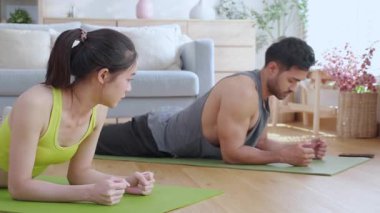 Genç Asyalı çift evdeki oturma odasında beşlik çakarken tahtayla antrenman yapıyor. Erkek ve kadın birlikte meydan okuma, motivasyon ve sağlık için kas gücü eğitimi alıyor..