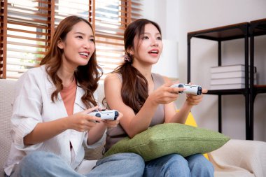 İki Asyalı kadın, evdeki rahat bir oturma odasında bilgisayar oyunu oynuyorlar. Eğlence, arkadaşlık ve neşeli bir yaşam tarzı. Asyalı arkadaşlar, eğlence ve oyun paylaşımının keyfini çıkarıyorlar..